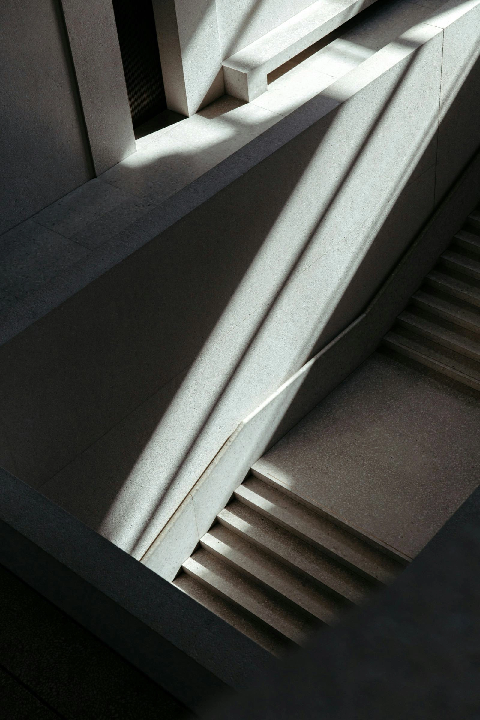 A modern concrete staircase illuminated by sunlight, casting sharp shadows..