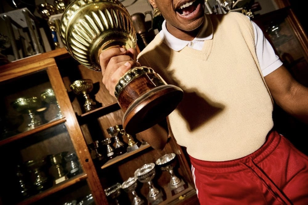 A boy holding a large trophy in front of a display case filled with multiple other trophies.