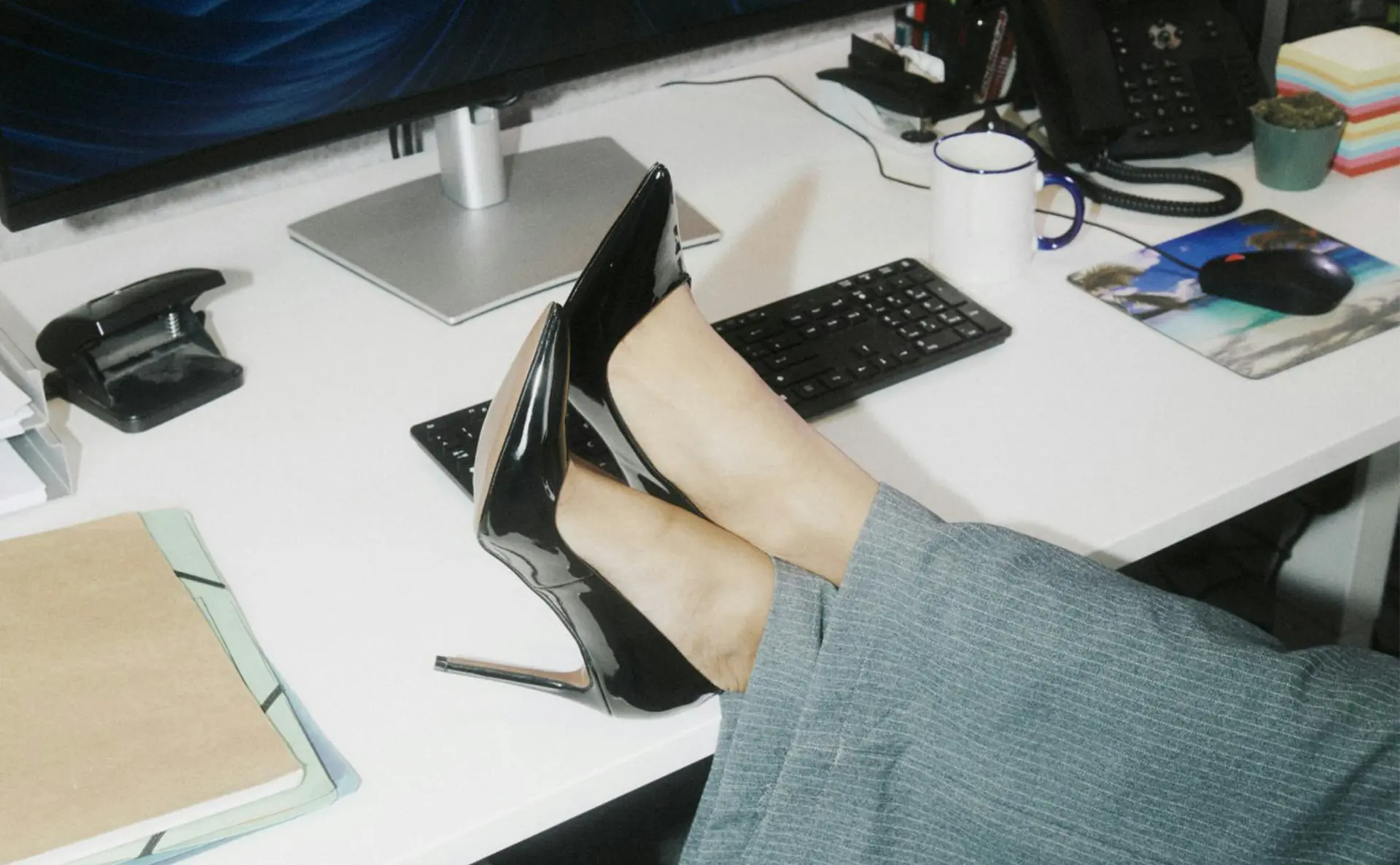 Business woman in high heels has her feet on the desk. A Keyboard and Computer can be seen in the background.
